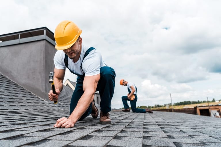 Roofer holding hammer while performing shingle repair on a residential roof